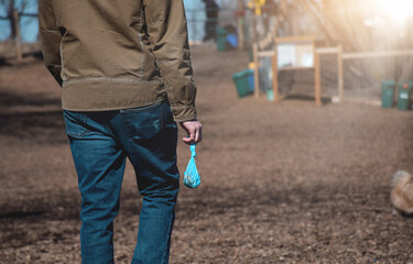 Man is carrying a dog poop bag to a garbage bin at an off leash dog park