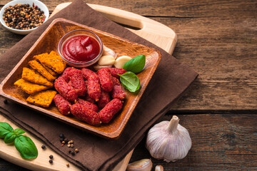 Wooden plate with smoked, garlic mini sausages and tomato crackers close-up on a brown wooden background.