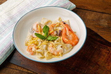 Pasta with shrimps in a creamy sauce, decorated with spinach on a gray plate on a wooden table on a napkin.