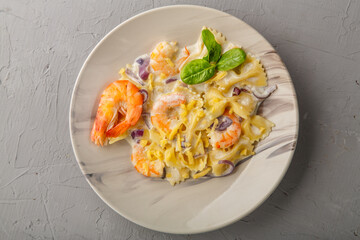 Pasta with shrimps in a creamy sauce on a gray plate on a concrete background.