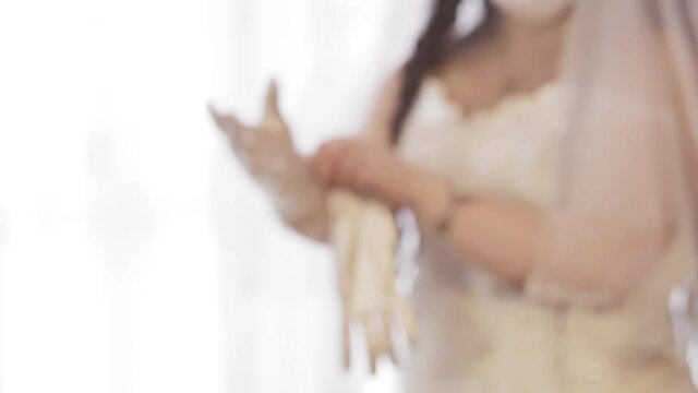 A Jewish bride in a wedding dress and a veil wearing a medical mask puts on elegant white gloves. From blur to sharpness