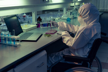 Disabled chemist in protective workwear and mask examining liquid in test tubes at the table in the lab