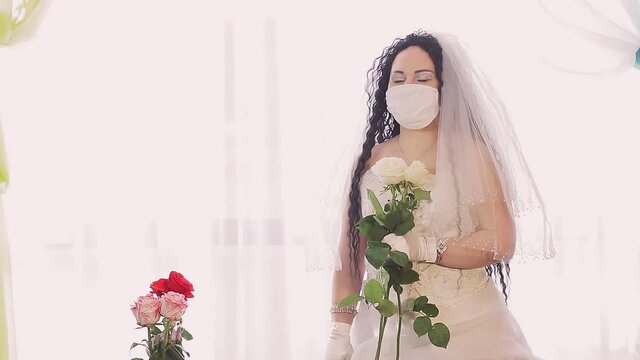 A Jewish bride in a wedding dress and a veil wearing a medical mask turns to the camera and looks for someone