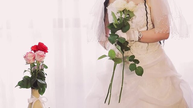 Jewish bride in a wedding dress and veil wearing a medical mask in the synagogue hall before the chupa ceremony with a bouquet of flowers
