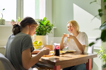 Teenagers guy and girl eating pancakes with jam, sitting at table at home
