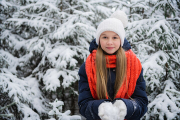 Fototapeta na wymiar A young teenage girl in a down jacket smiles beautifully for a picture in a winter snow covered forest