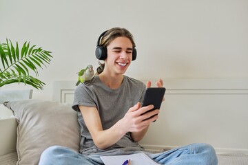 Male teenager in headphones with smartphone using video call, parrot on shoulder © Valerii Honcharuk