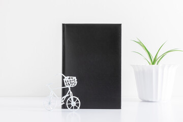 Office white table. Mock up book blank black, leather cover for magazine, booklet, brochure, diary, green plant in pot on white background. Front view. Place for text, copy space, mockup