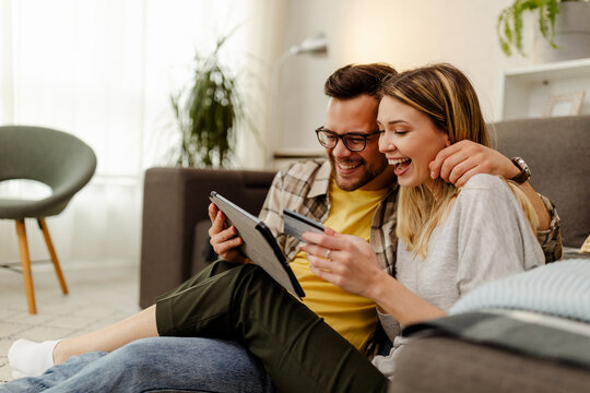 Image of excited cheery young loving couple at home on floor near sofa using laptop computer.