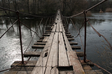 Obraz premium Wooden suspension bridge on the river. Springtime.
