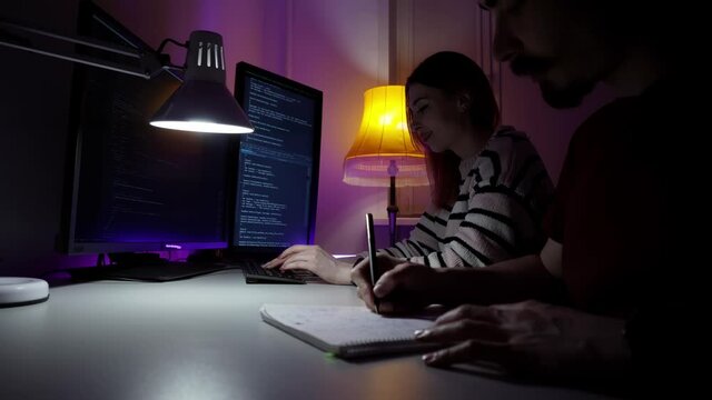 Two young caucasian programmers are sitting in front of computer and developing new software in process of discussion. A woman is typing new html code lines on keyboard and a man is sharing his ideas.