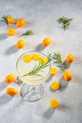 Gin and tonic cocktail with kumquat fortunella in glass of champagne on light gray table surface.