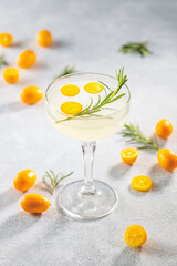 Gin and tonic cocktail with kumquat fortunella in glass of champagne on light gray table surface.