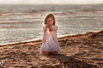 Cute little blond girl playing with falling sand at the beach in sunset