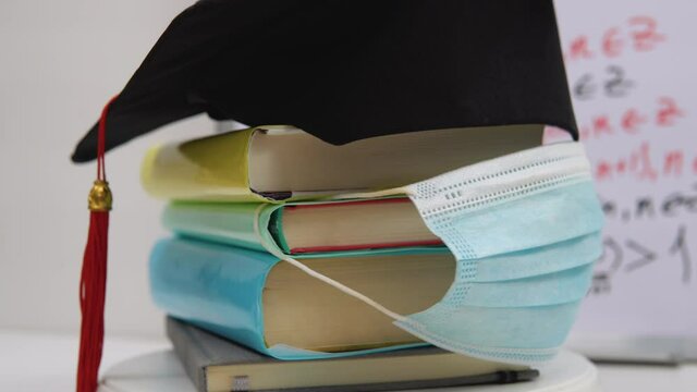 The black square hat of the master lies on the textbooks stacked in a column and decorated with a protective medical mask. The attributes of a university graduate revolve around its axis on a stand