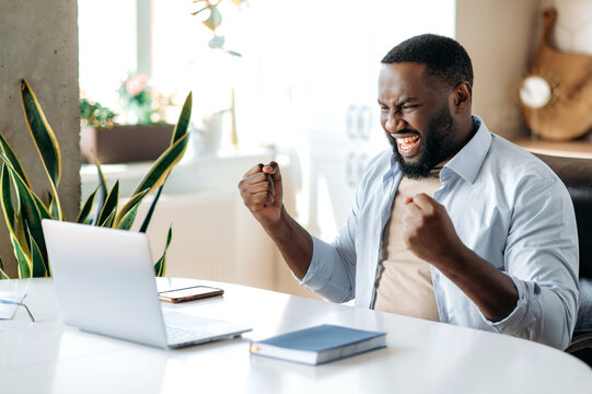Happy confident friendly african american business leader, broker or manager working remotely, looking at laptop, received a good message or made a good deal, gesturing with his hands, smiling - Powered by Adobe