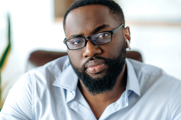 Close-up portrait of an attractive confident successful intelligent serious african american bearded man with glasses, wearing a stylish formal shirt, concentrated looking at the camera