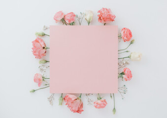 Creative layout made of pink flowers and leaves with paper card note. Flat lay. Nature concept