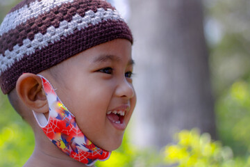 Portrait Asian little boy with hat, nice smiling with happy headshot blurred background close up view with copy space, concept little boy Muslim lifestyle outdoor,