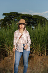 Young latin woman farmer with serious expression looking right at the camera, posing in front of the sugarcane crop. Agriculture and cultivation concept