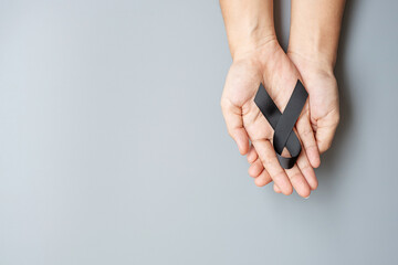 Fototapeta premium Melanoma and skin cancer, Vaccine injury awareness month and rest in peace concepts. Man holding black Ribbon on grey background