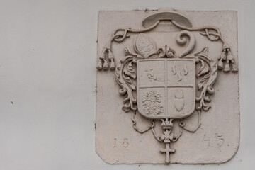 The old coat of arms of 1843 on the wall of the house. Coat of arms with papal hat, cross and...