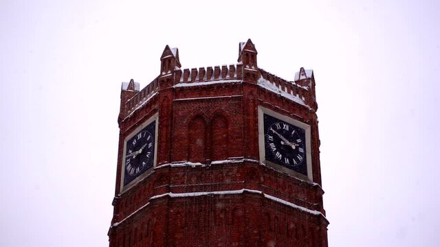 Big old brick tower with clock in snowfall in winter, slow motion