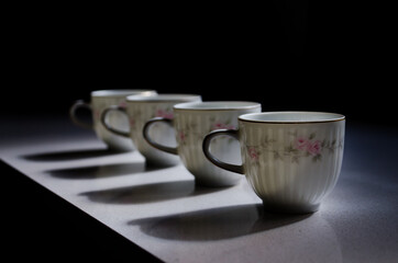 Perspective of four porcelain coffee cups on dark background, selective focus.