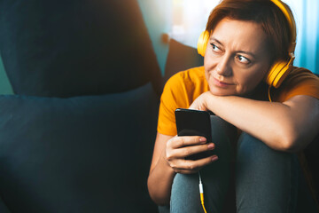 Woman with headphones at home on the couch. Listening to a podcast or live broadcast. 