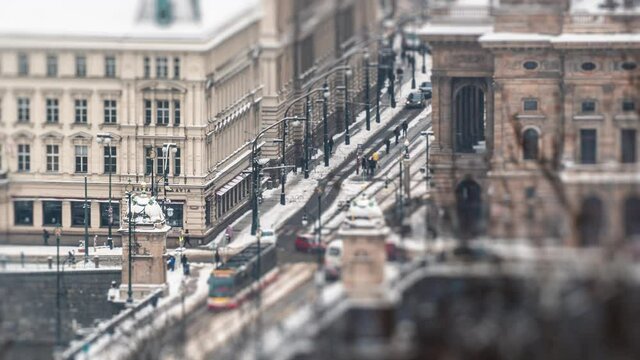 Prague urban landscape. Fresh snow covering the ground, roofs, roads, and tram tracks. Cars, trucks, and trams moving to their destinations. Pedestrians hurrying busily about their business.