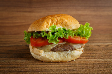 Delicious hamburger on wooden background. Burger with tomato, lettuce, meat and cheese.