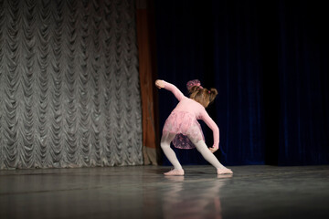 A girl in a pink dress is dancing on the stage. A child from a dance school. The girl shows dance moves.