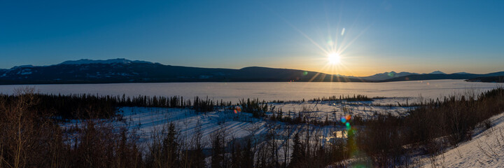 Sunset above a fully frozen lake in northern Canada with perfect blue sky, wilderness setting below of snow covered landscape on Little Atlin Lake, Yukon. 
