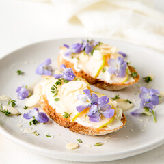 elegant bruschettas with cream cheese, pear, thyme, almonds and edible violets flowers on a white...