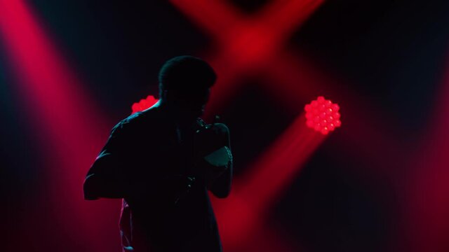 Happy smiling black man bangs on talking African yuka drum and dances in a dark studio against a background of red lights. Silhouette of an African American musician. African ethnic music.