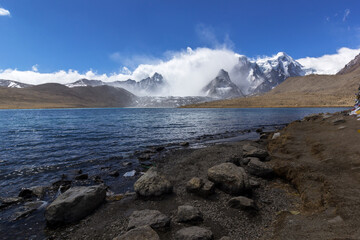 landscape of Gurudongmar Lake with rocks in forte ground and mountain with blue sky in background. Gurudongmar lake one of the highest lake of the world and India.
