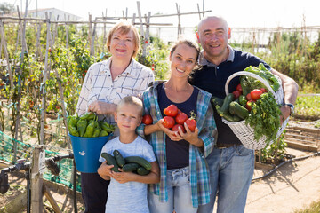 Portrait of positive family of gardeners standing in garden with gathered vegetables