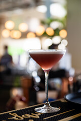 Cocktail waitress prepares and pours a pink cocktail in a elegant tall glass with a bustling blurred bright resort in the background 