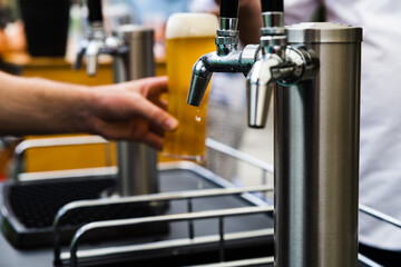 Silver Beer taps with black handles covered in condensation with a hand serving a tall glass of amber coloured beer in the background with a perfect head 
