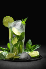 Fresh homemade mojito cocktail in a tall glass with lime, mint and ice on a black background, copy space, vertical image