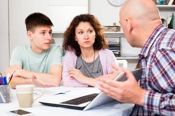 Young woman with her husband and teen son calculating domestic budget at table ..