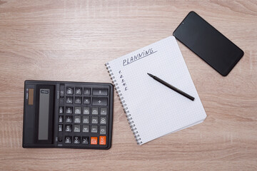 The word planning is written in a notebook next to a smartphone, a calculator on the table