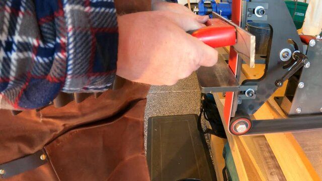 Man using a belt grinder to clean up bar steel stock to make a knife - isolated close up