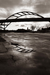 bridge over the river reflected in puddle on pavement in black and white
