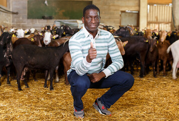 Portrait of happy successful African-American man professional goat breeder in stall on goat farm