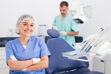 Portrait of a positive young female dentist in uniform with crossed hands at the dental office