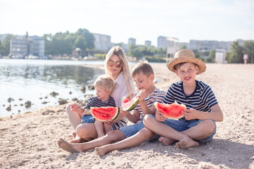 Fototapeta na wymiar Happy family, mother with three sons resting in the beach with fruits, people dressed in t-shirts