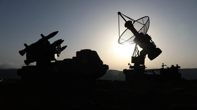 Creative artwork decoration. Silhouette of mobile air defence truck with radar antenna during sunset. Rocket launcher aimed at sky ready to attack. Selective focus