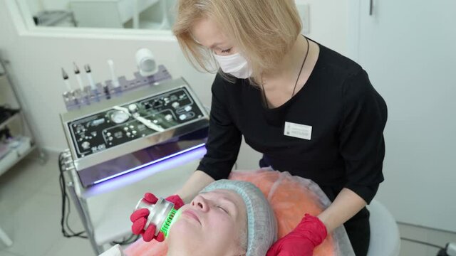 Ultrasonic massager. Light skin treatment. A woman in a beauty salon undergoes a course on facial skin rejuvenation.