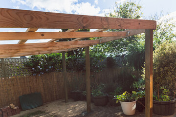 under construction garden pergola with wooden structure in sunny backyard surrounded by tropical plants